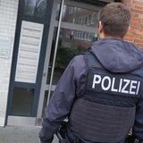 Ein Polizist steht vor einem Haus, in dem eine Wohnung durchsucht werden soll.