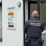 Ein Polizeibeamter steht vor der Tür der m-haditec Gmbh während einer Durchsuchung der Geschäftsräume in Bremen-Huchting.