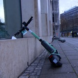 Ein Grüner E-Scooter lehnt schräg an einem Gebäude.