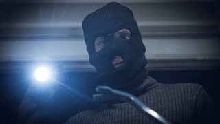 Ein maskierter Einbrecher hebelt mit Brecheisen ein Fenster auf und bricht bei Nacht in ein Haus ein.