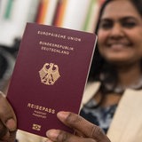 Eine aus Indien stammende junge Frau hält während einer Einbürgerungsfeier lachend ihren deutschen Reisepass in die Kamera.