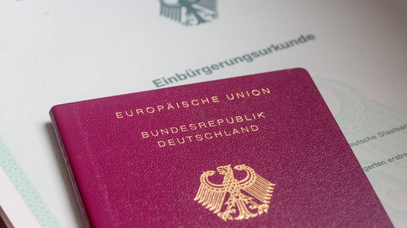 Eine Einbürgerungsurkunde der Bundesrepublik Deutschland und ein deutscher Reisepass liegen auf einem Tisch. 