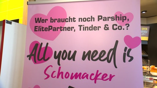 Ein rosa Schild mit Herzen und Aufschrift in einem Supermarkt.