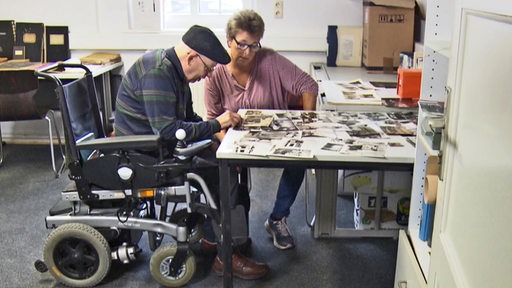Ein alter Mann in einem Rollstul guckt sich gemeinsam mit einer Frau Bilder in einer Pflegeeinrichtung an.
