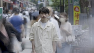 Ein Japaner steht in einer Masse von Menschen, die an ihm vorbeigehen.