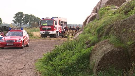 Im Vordergrund sind Strohballen zu sehen. Im Hintergrund stehen Feuerwehrleute.