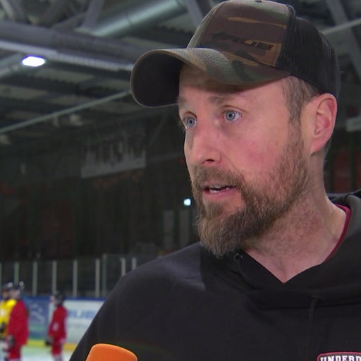 Eishockey-Coach Andrew McPherson steht auf dem Eis bei einem Interview.