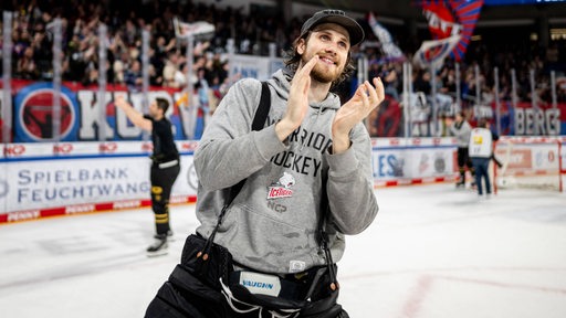 Der Eishockey-Torwart der Nürnberg Ice Tigers, Leon Hungerecker, steht nach einem Spiel strahlend im grauen Kapuzenpulli auf dem Eis und applaudiert den Fans.