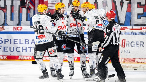 Eishockey-Spieler der Fischtown Pinguins stehen in weißen Trikots auf dem Eis und umarmen sich im Torjubel.