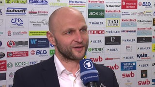 Eishockey-Manager Sebastian Furchner von den Fischtown Pinguins steht vor einer Werbewand beim Interview nach dem Sieg gegen Köln.