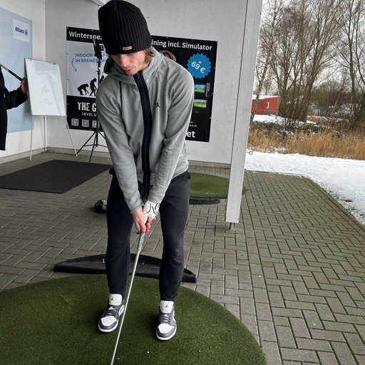 Eishockey-Profi Ziga Jeglic steht in einem Golfklub in der Driving Range und konzentriert sich auf den Abschlag.