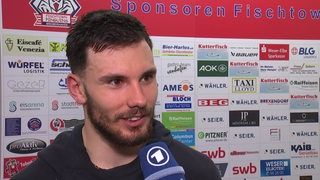 Eishockey-Spieler Nino Kinder von den Fischtown Pinguins steht vor einer Werbewand beim Interview nach dem Sieg gegen Köln.