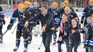 Eishockey-Spieler der Fischtown Pinguins starten neben Manager Alfred Prey auf dem Eis eine Welle mit den Fans.
