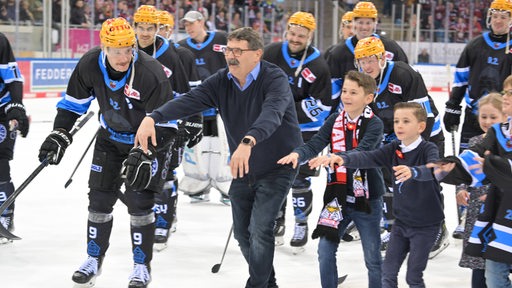 Eishockey-Spieler der Fischtown Pinguins starten neben Manager Alfred Prey auf dem Eis eine Welle mit den Fans.