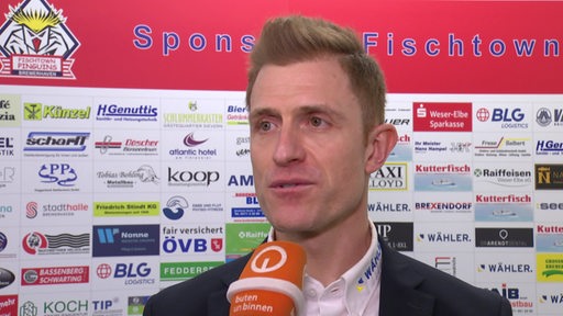 Eishockey-Trainer Alexander Sulzer von den Fischtown Pinguins steht nach der Niederlage im ersten Play-off-Spiel vor einer Werbewand beim Interview.