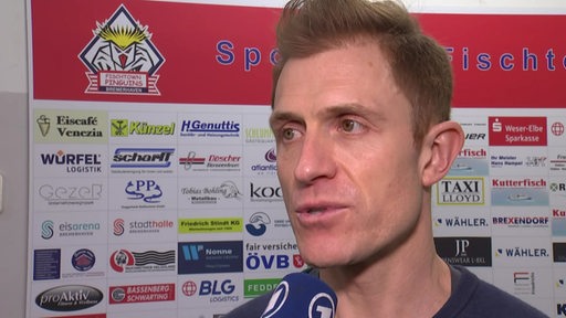 Eishockey-Trainer Alexander Sulzer von den Fischtown Pinguins steht vor einer Werbewand beim Interview nach dem Sieg gegen Köln.