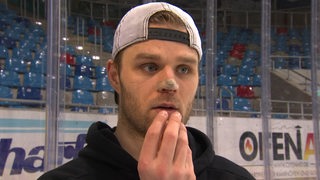 Eishockey-Profi Christian Wejse von den Fischtown Pinguins steht mit Pflaster auf der Nase auf der Eisfläche und erklärt, wie die Verletzung passiert ist.