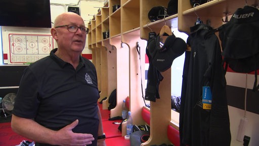 Eugen Witthohn, der Zeugwart der Fischtown Pinguins, steht in der Kabine der Eishockey-Profis und erklärt den neuen Halsschutz in der Ausrüstung.