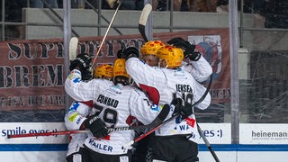 Eishockey-Spieler der Fischtown Pinguins umarmen sich an der Bande beim Torjubel gegen München.