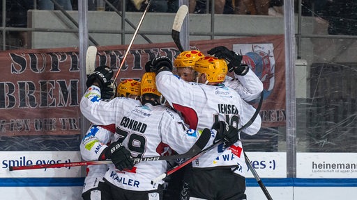 Eishockey-Spieler der Fischtown Pinguins umarmen sich an der Bande beim Torjubel gegen München.