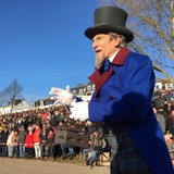 Ein Mann in Frack und mit Zylinder steht am Weserdeich. Im Hintergrund schauen ihm Hunderte Menschen auf dem Deich zu.