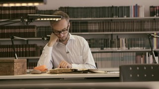 Jan Böhmermann sitzt im Lesesaal eines Archivs