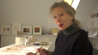 Die Künstlerin Elke Hellas Markopoulos sitzt in ihrem Atelier und arbeitet an ihrern Werken.
