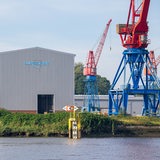 Die ehemalige Elsflether Werft an der Hunte mit Gebäuden mit Logo und Kränen die aufs Wasser herausragen
