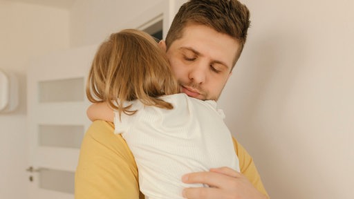 Ein Vater hält sein Kind im Arm und tröstet es (Symbolbild)