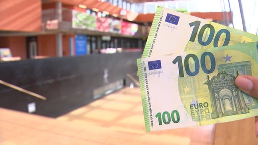 Eine Person hält zwei 100 Euro Scheine in der Universität Bremen in der Hand. 