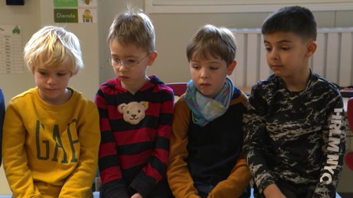 Vier Erstklässler sitzen in einer Reihe im Unterricht und schauen traurig nach unten.