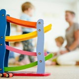 Eine Erzieherin spielt in einer Kindertagesstätte hinter einer Rollbahn mit Kindern.