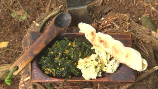 Gekochter Spinat mit Rührei und Stockbrot auf einem Holzbrett.