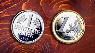 Eine 1-DM-Münze  und eine 1-Euro Münze liegen auf einem Holzuntergrund