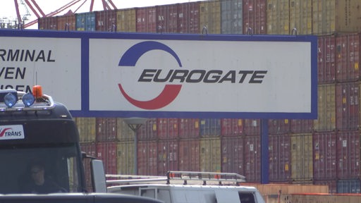 Auf einem Schild steht groß "Eurogate" drauf und im Hintergrund ist eine Wand aus Containern zu sehen. 