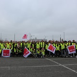 Menschen mit Warnwesten und Fahnen posieren auf einem Parkplatz für ein Gruppenfoto.
