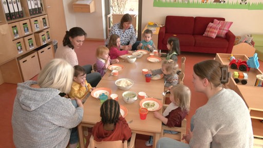 Erzieherinnen und KiTa-Kinder an einem Tisch beim Mittagessen.