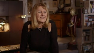 Modedesignerin Evelyn Frisinger in ihrer Wohnung im Interview mit einem Bücherregal im Hintergrund