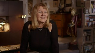 Modedesignerin Evelyn Frisinger in ihrer Wohnung im Interview mit einem Bücherregal im Hintergrund