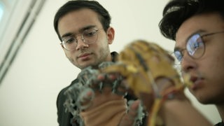 Es ist der Student und Entwickler Zain Samdani zu sehen. Im Vordergrund sieht man ein Exoskelett.