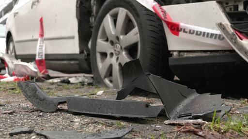 Plastikteile eines Autos vor einem platten Reifen und Polizeiabsperrband.