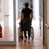 Eine Pflegerin schiebt einen Patienten im Rollstuhl.