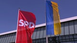 Die Fahne der SPD und die Flagge der Ukraine, vor blauem Himmel.