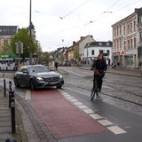 Ein Fahrrad fährt gefährlich vor einem Auto auf dem Fahrradweg.