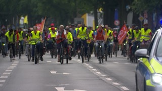 Viele Fahrradfahrer sind zusammen auf einer Demonstration. Viele tragen neongelbe Warnwesten oder haben Fahnen mit dabei.