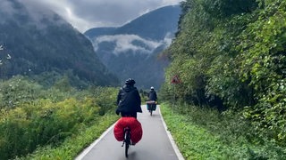Fahrradreisende auf einem Radweg vor wolkenverhangenen Bergen