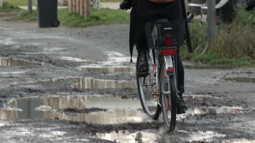 Ein Fahrrad auf einer sehr kaputten Straße mit großen Schlaglöchern.