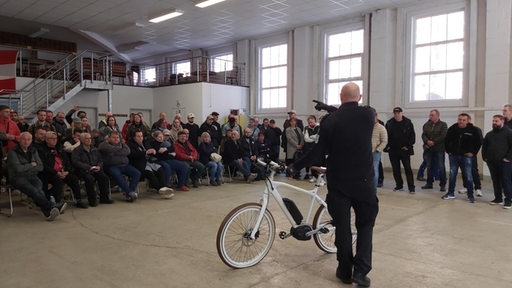 Ein Mann mit einem Fahrrad steht vor einer größeren Gruppe Menschen.