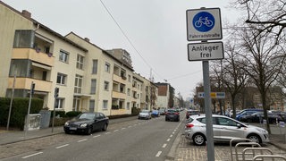 Blick in eine Straße. Im Vordergrund steht ein Schild mit den Hinweisen "Fahrradstraße" und "Anlieger frei".