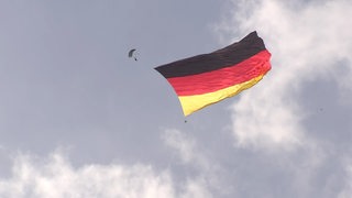 Fallschirmspringer mit einer riesigen Deutschlandflagge am Himmel.